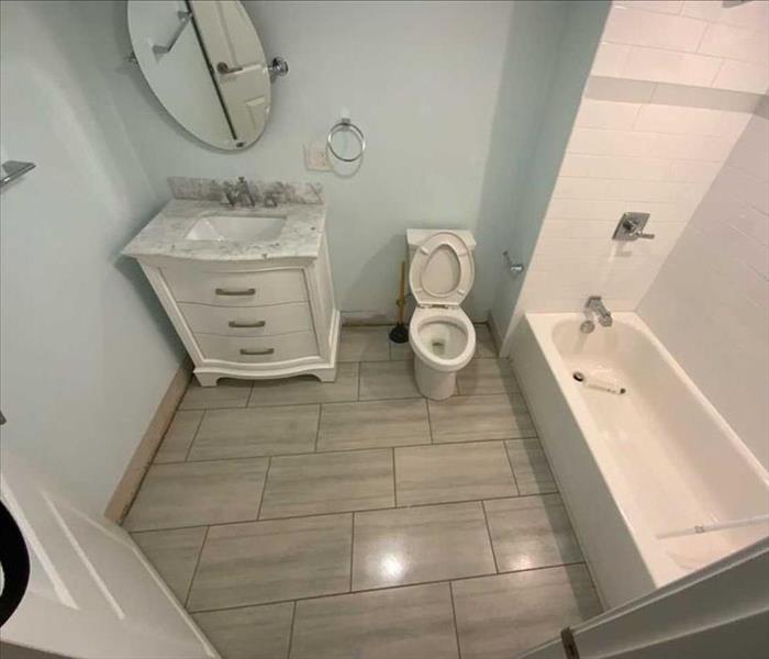 A clean bathroom with a clean shower curtain rod in the bathtub that only needs new baseboards to complete the room