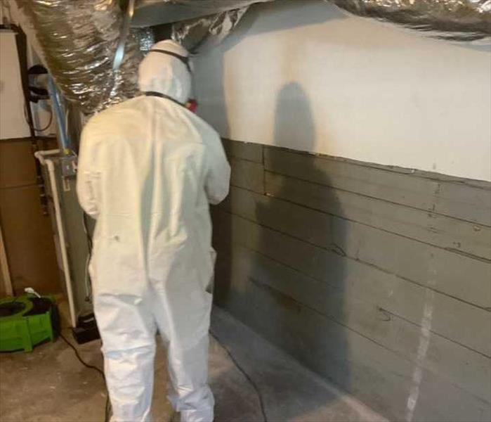 tech wearing white Tyvek suit and spraying