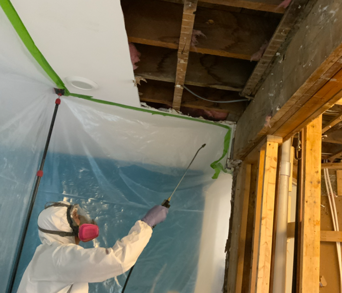 tech in ppe applying spray to ceiling
